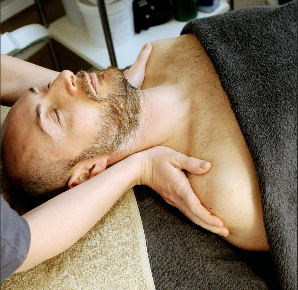 Hands placed on the shoulders of a man on massage table